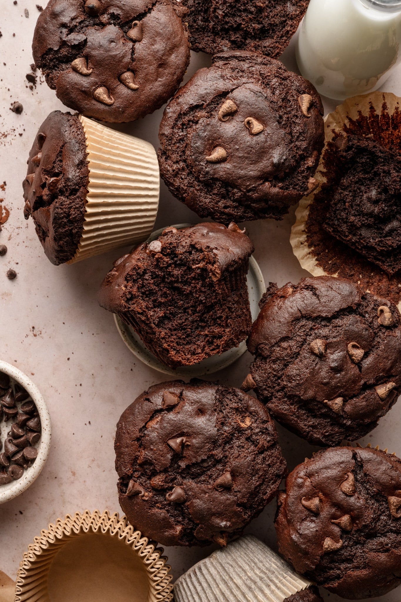 Plate of double chocolate muffins on board with glass of milk and bowl of chocolate chips on the side.