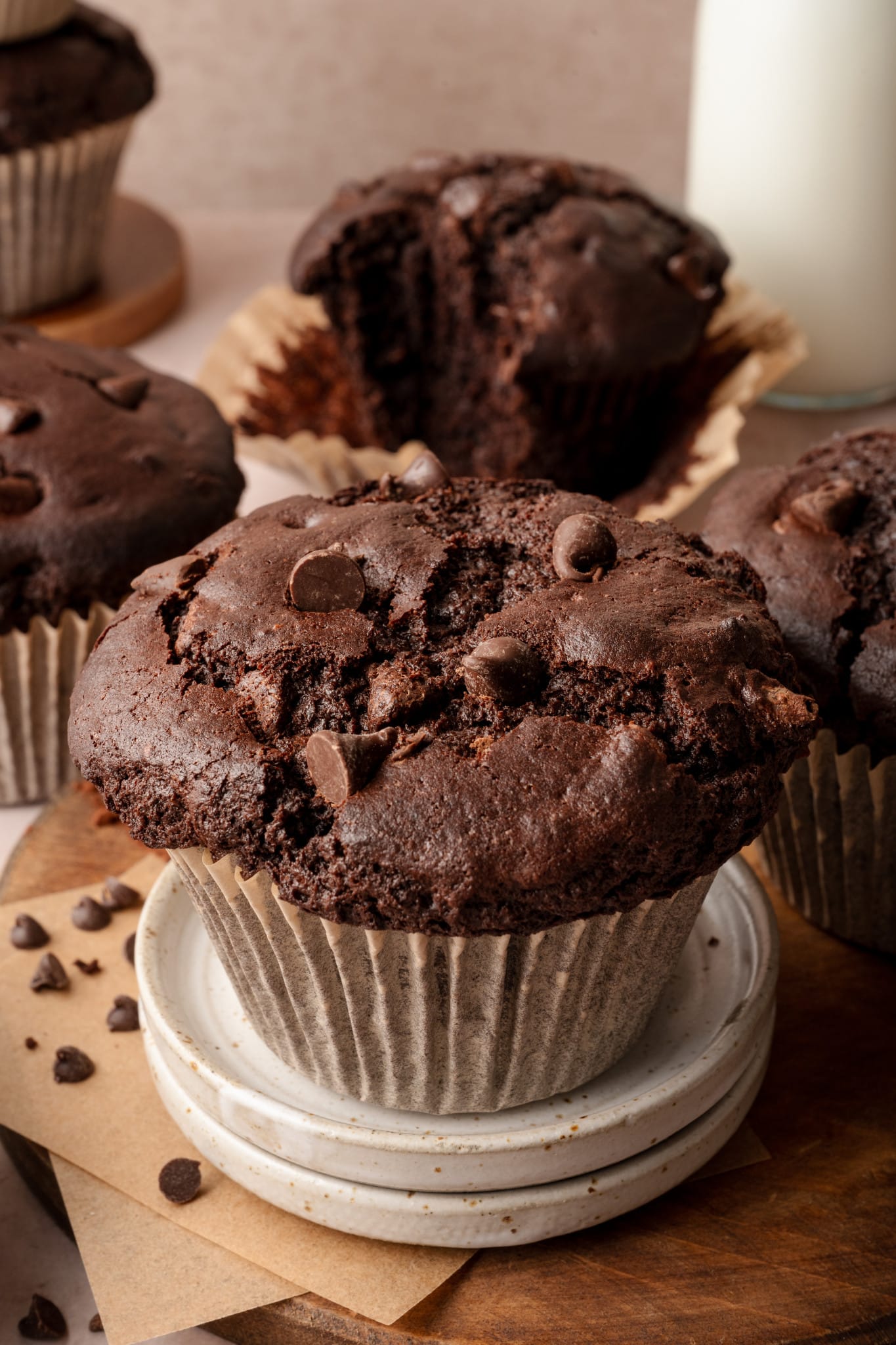 Image of double chocolate bakery-style muffin in paper liner on top of two mini serving plates and 4 muffins in the background.