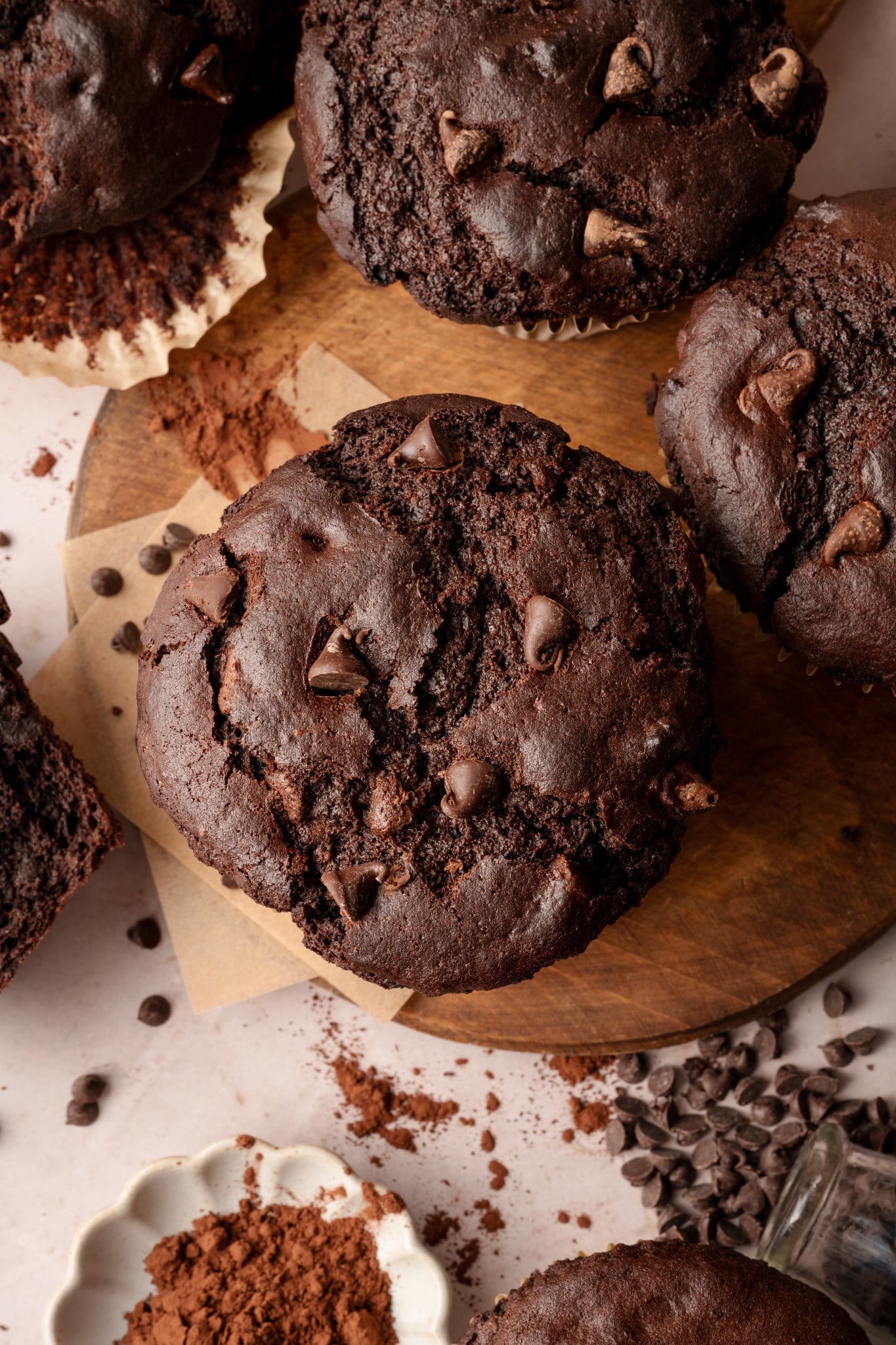 Aerial shot of the top of oversized, jumbo chocolate muffin on wood board with remaining muffins surrounding it.