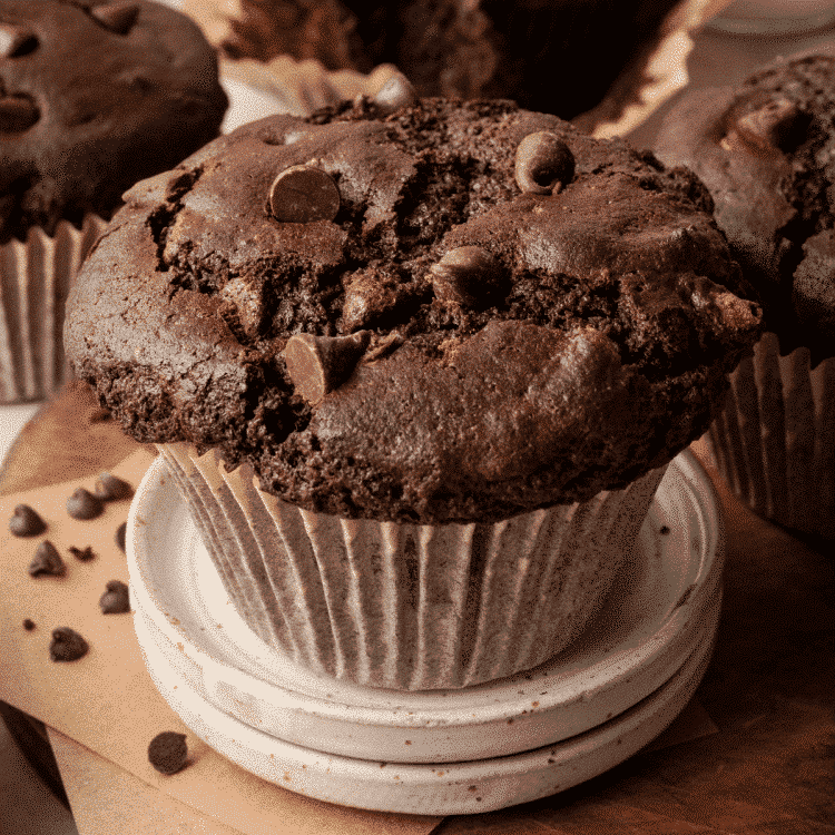 Featured image Aerial shot of the top of oversized, jumbo chocolate muffin on wood board with remaining muffins surrounding it.