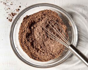 Dry ingredients for double chocolate muffins whisked together in clear mixing bowl with whisk.