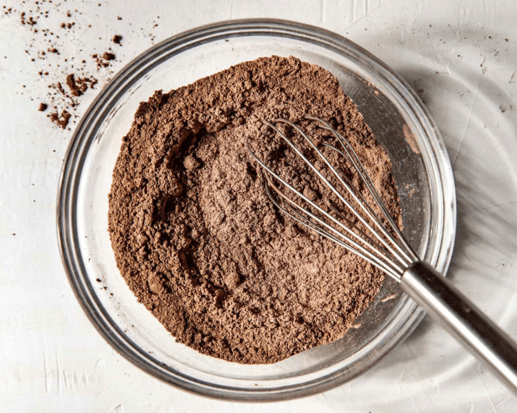 Dry ingredients for double chocolate muffins whisked together in clear mixing bowl with whisk.