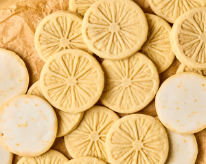 Picture of lemonade cookies after they have been baked and dipped into the glaze. Picture is showing the top of some of the cookies with the lemon stamp and the other cookies are turned over to show glaze on the bottom.