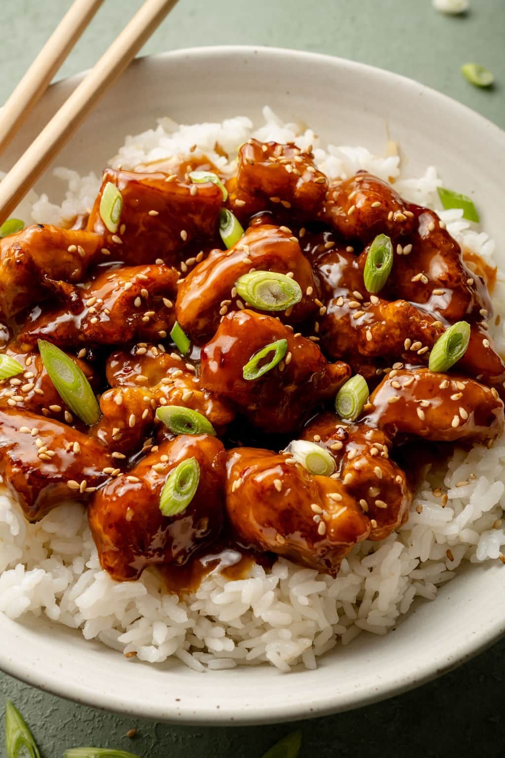 Panda express orange chicken on top of white rice in bowl garnished with green onions and chop sticks on the side.