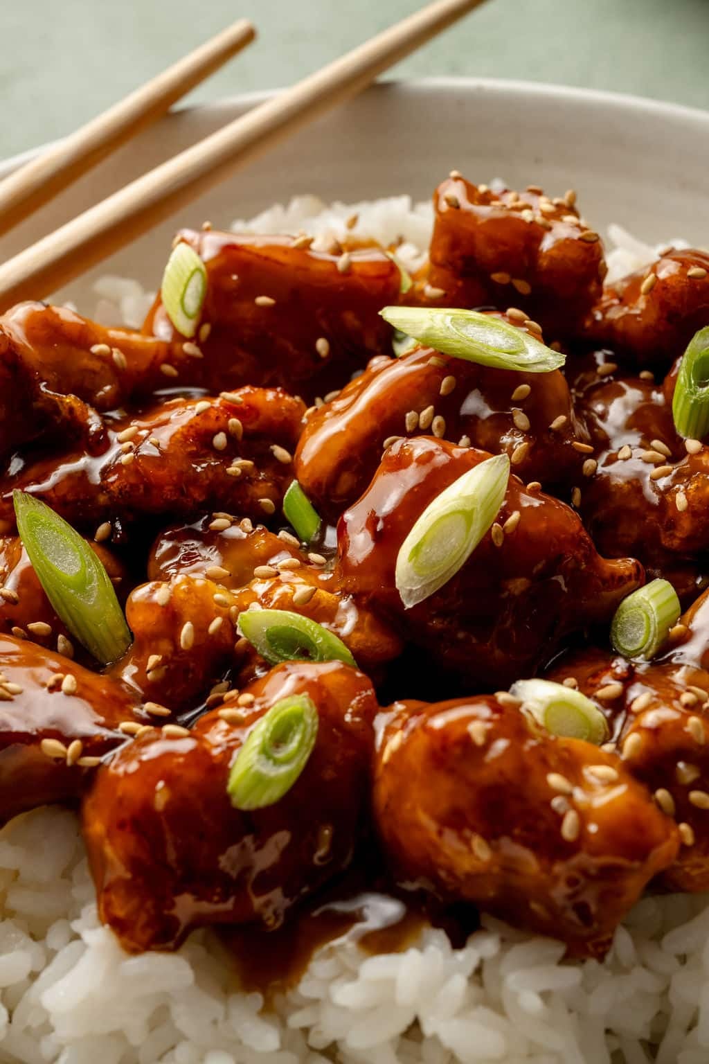 Upclose shot of crispy panda express orange chicken on top of white rice in bowl with chopsticks on the side.