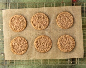 Freshly baked oatmeal cookies cooling on parchment-lined wire rack, evenly golden and slightly crinkled on top.