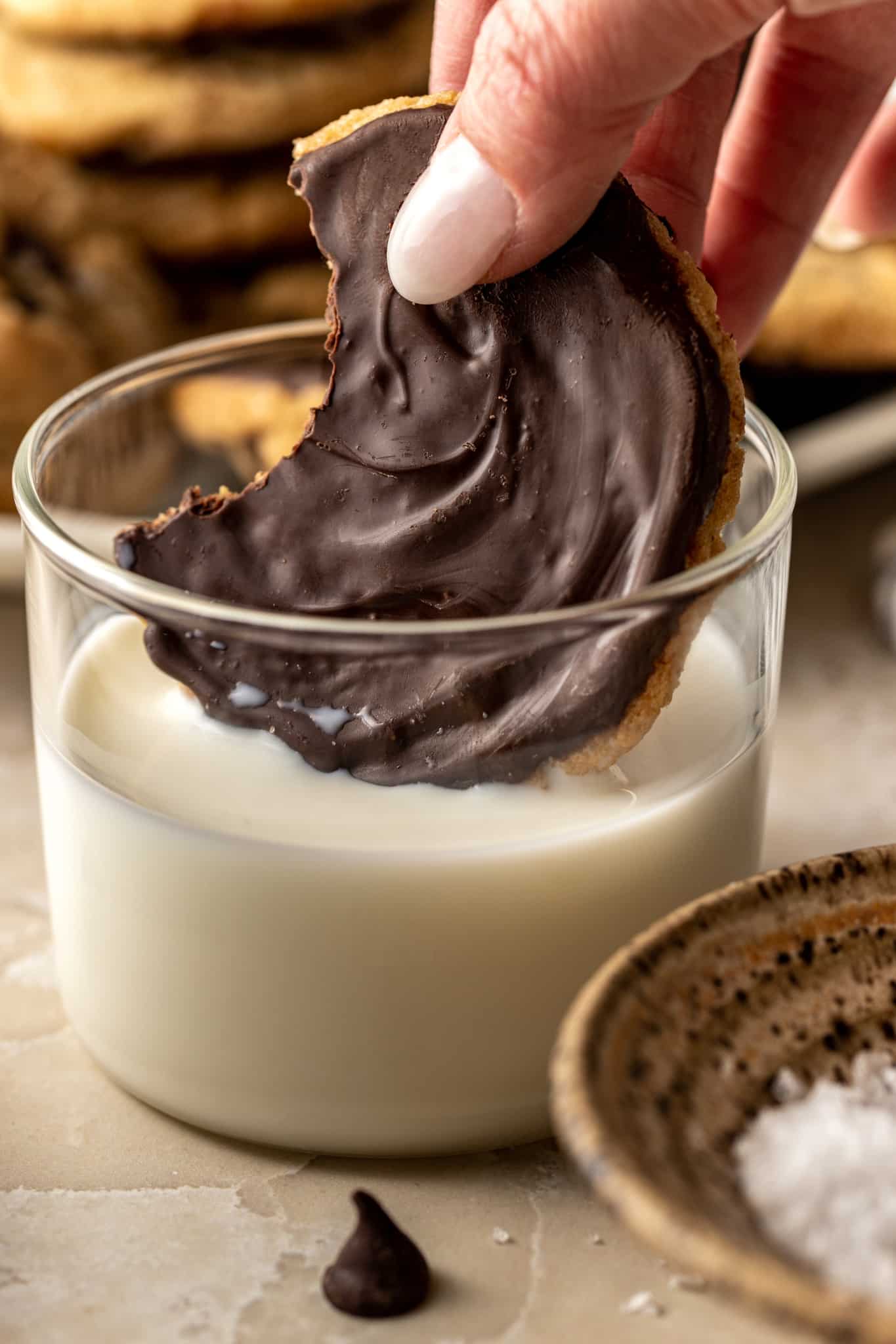 Hand dipping a chocolate dipped cooking in a glass of milk and a bite taken out of the cookie.