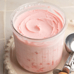 Ninja Creami Strawberry Frozen Yogurt in creami pint container on cream plate with ice cream scoop beside it.