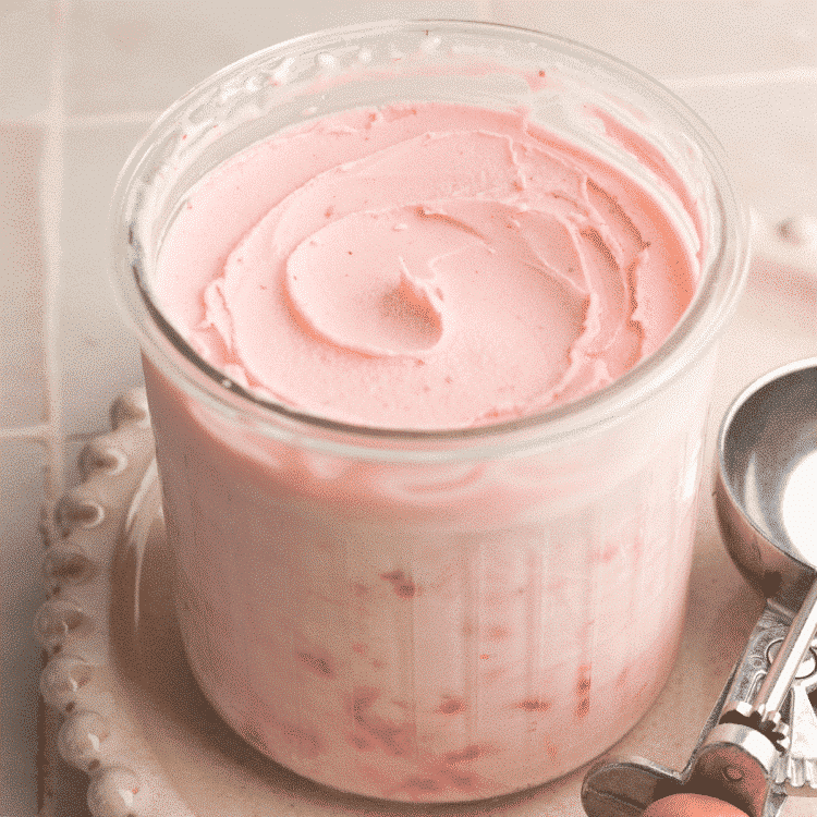 Ninja Creami Strawberry Frozen Yogurt in creami pint container on cream plate with ice cream scoop beside it.