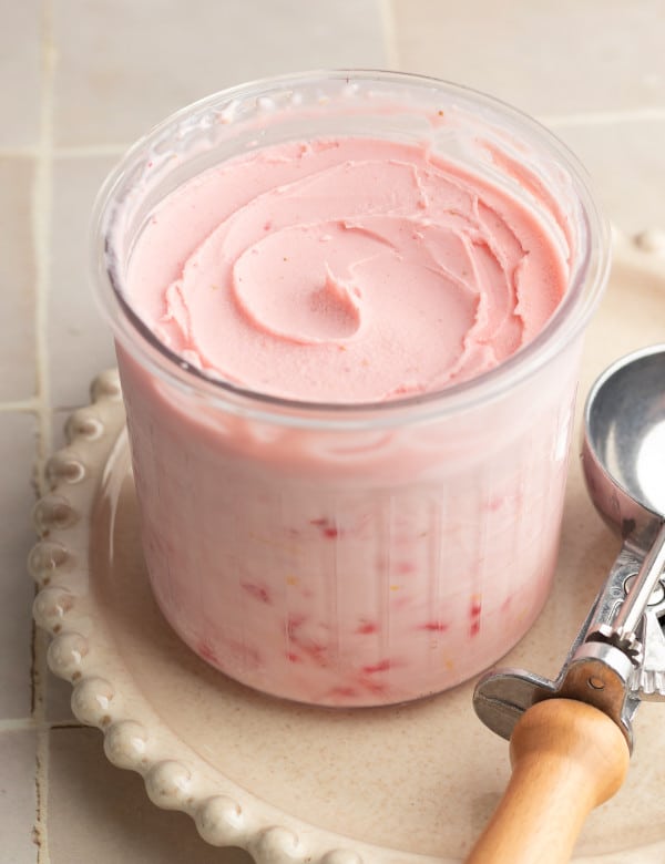 Ninja creami strawberry frozen yogurt in pint container after spinning on cream plate with ice cream scoop beside it.