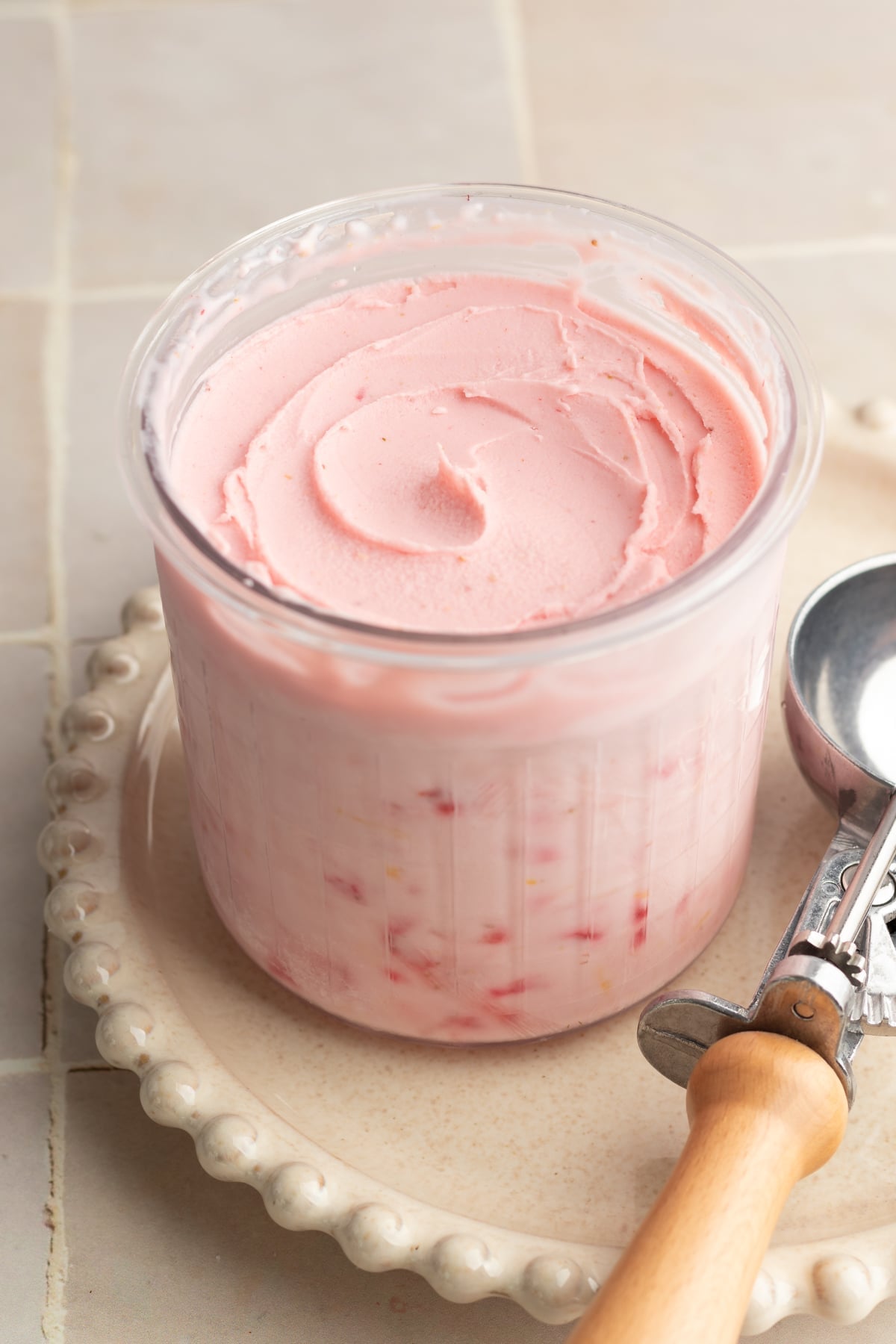 Ninja creami strawberry frozen yogurt in pint container after spinning on cream plate with ice cream scoop beside it.