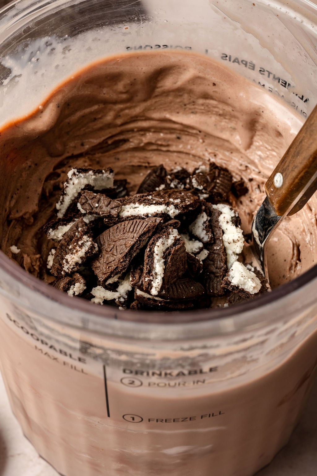Close-up of creamy chocolate protein ice cream inside a Ninja Creami container, topped with crushed Oreo cookies, ready to be mixed in.
