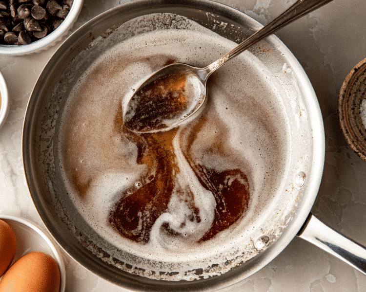 Brown butter melted in metal pan with spoon.