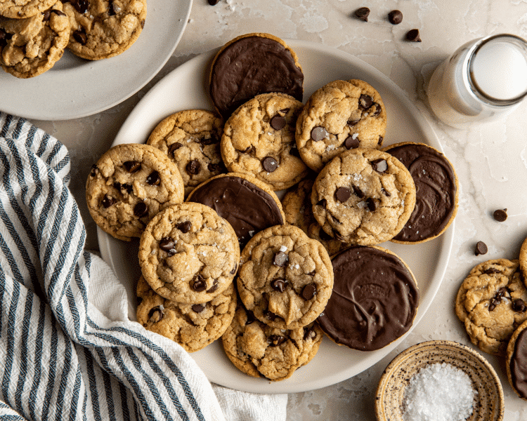 Plate of chocolate dipped brown butter cookies with glass of milk and stripped towel on the side.