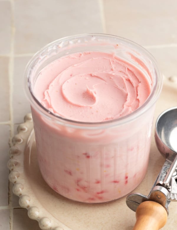 Ninja creami strawberry frozen yogurt in pint container after spinning on cream plate with ice cream scoop beside it.