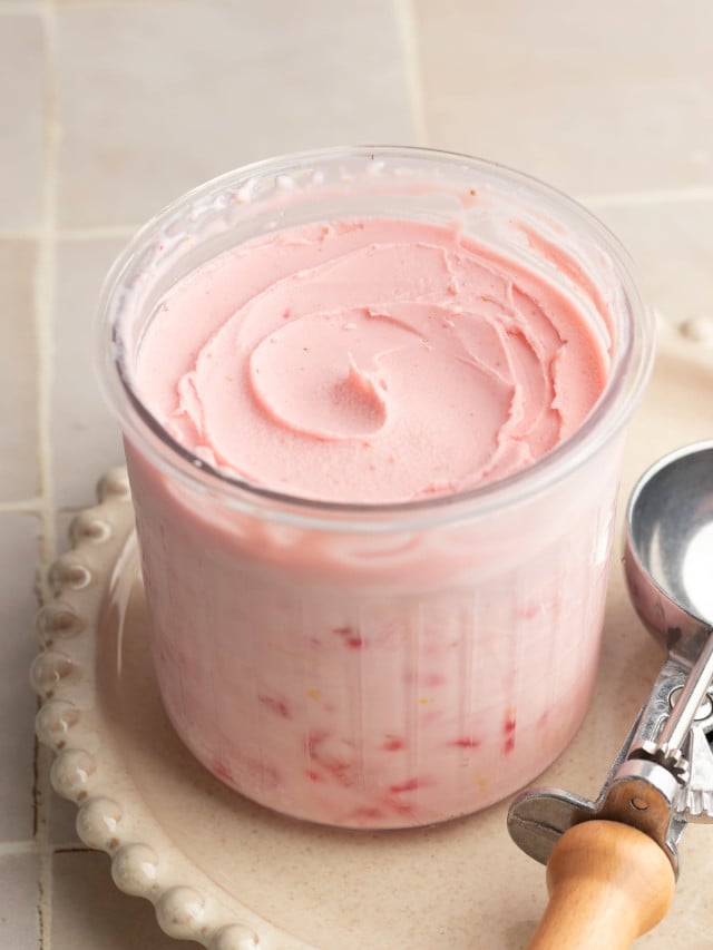 Ninja creami strawberry frozen yogurt in pint container after spinning on cream plate with ice cream scoop beside it.