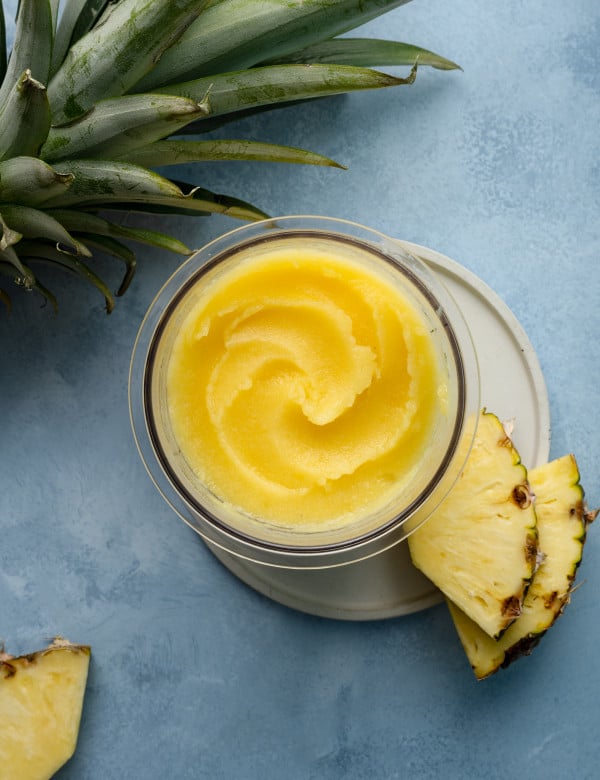 Ninja creami pineapple sorbet in pint container on plate garnished with two pineapple chunks.