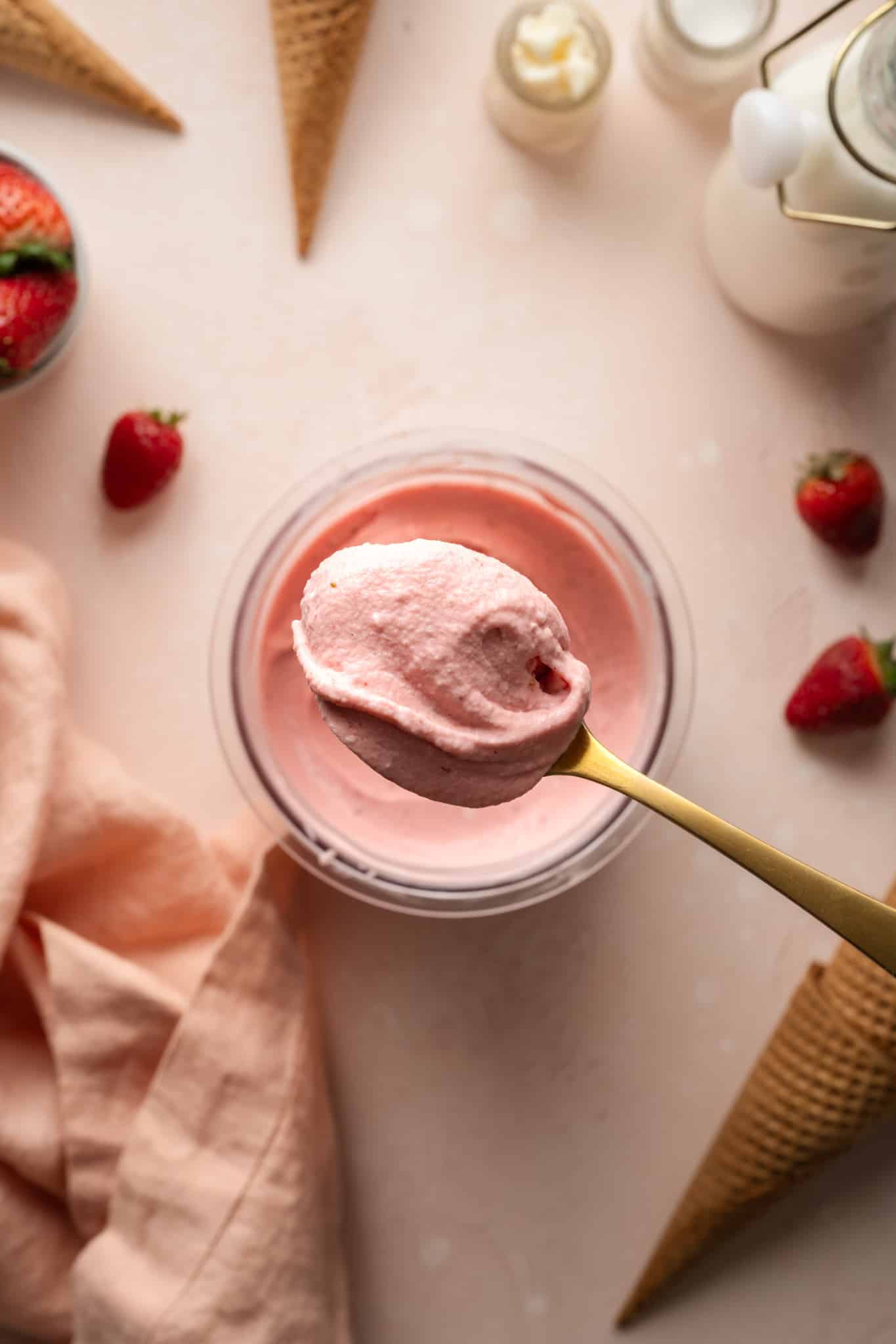 Strawberry ice cream on gold spoon with the pint container below it.