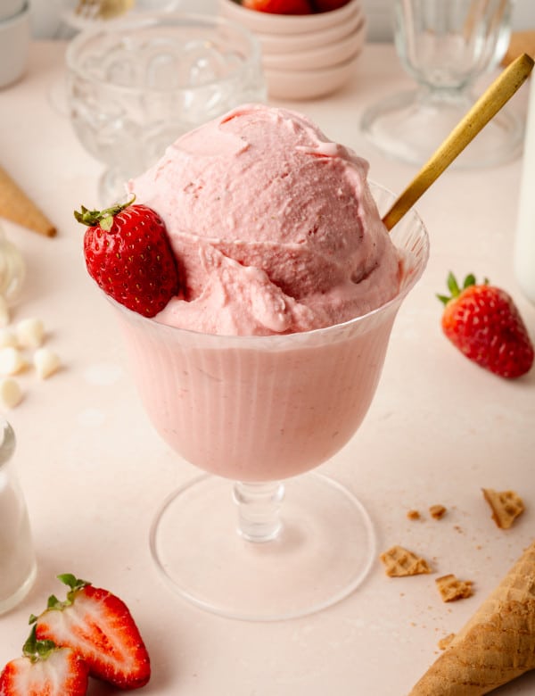 Strawberry ice cream (ninja creami) in glass bowl with gold spoon and fresh strawberry on the side.