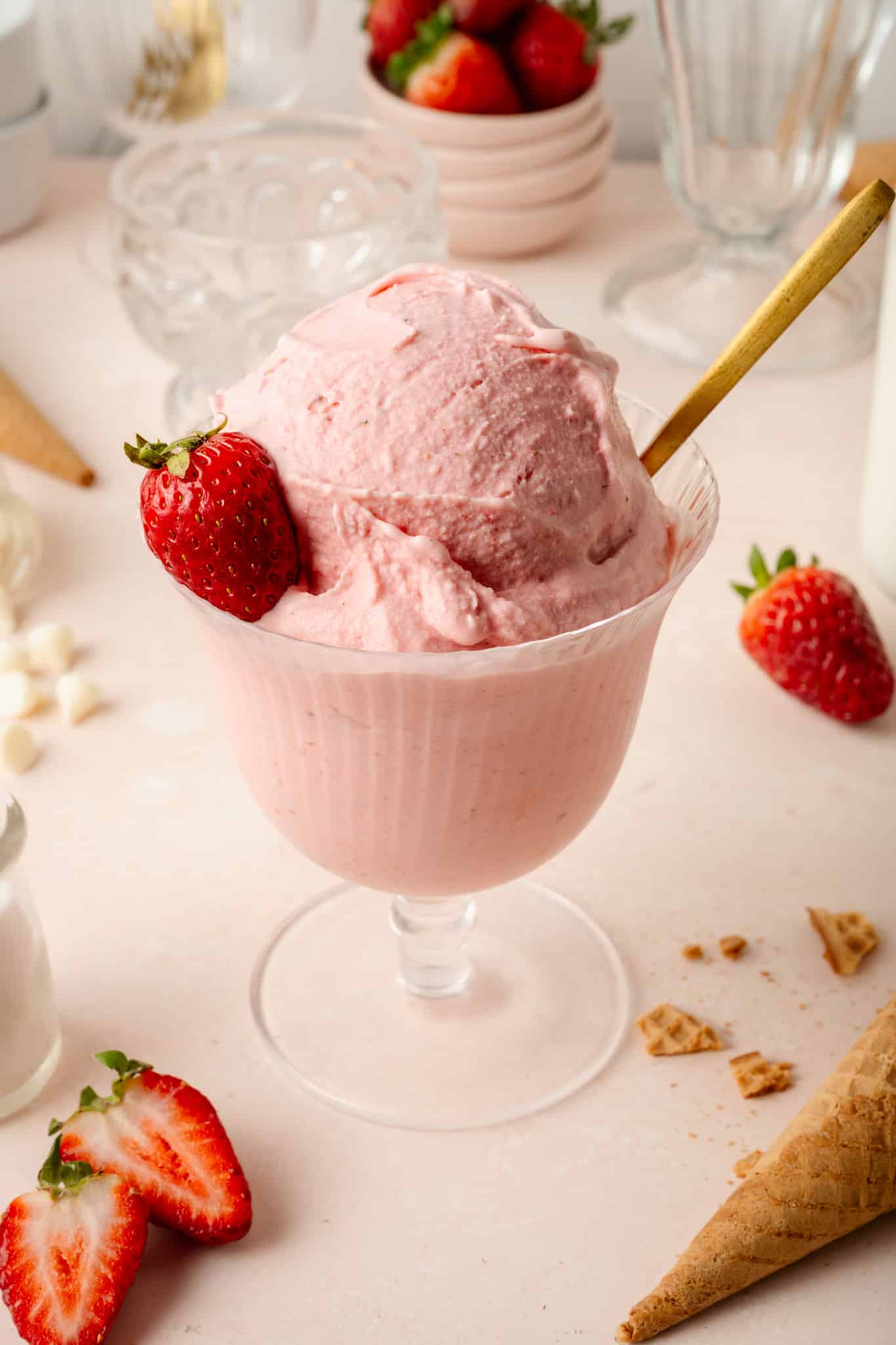 Strawberry ice cream (ninja creami) in glass bowl with gold spoon and fresh strawberry on the side.