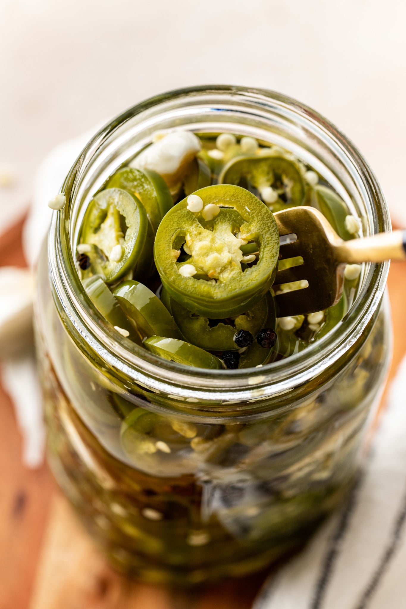 Pickled jalapenos in glass mason jar with gold fork lifting jalapeno out of jar.