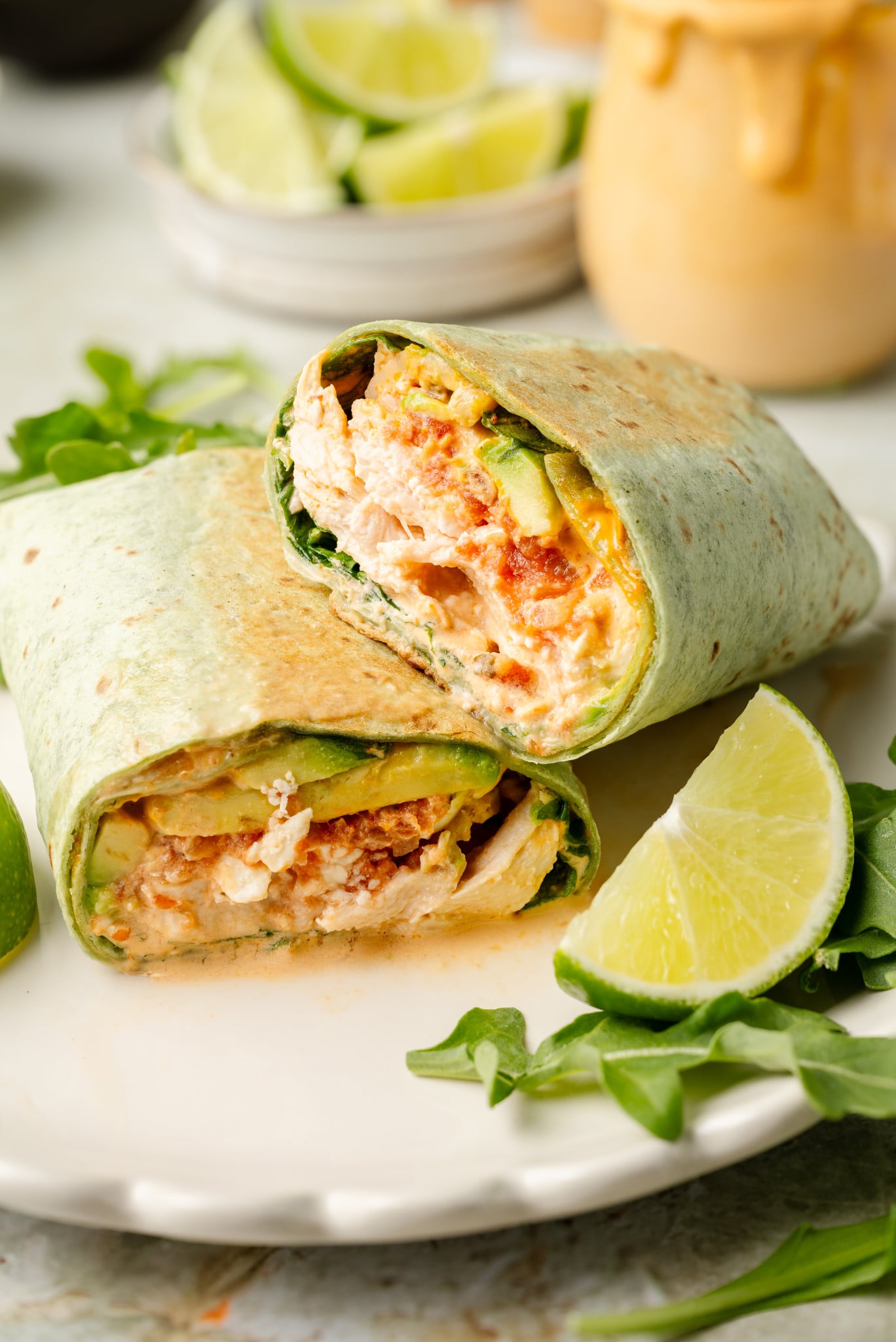 Chipotle chicken wrap sliced in half and stacked on plate with arugula and lime garnish on plate.
