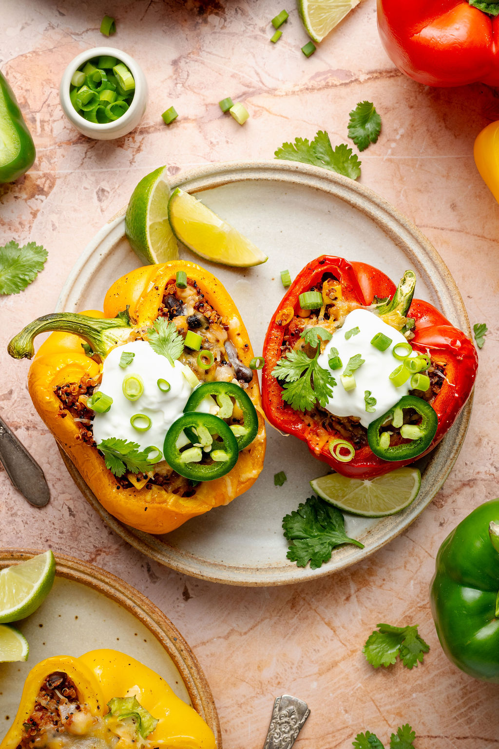 A baking dish filled with roasted red, yellow, and orange bell pepper halves stuffed with quinoa mixture, topped with shredded cheese ready to be melted.