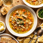 Two bowls of Lemon Chicken soup in bowls with bread, spoons, and parsley surrounding them.
