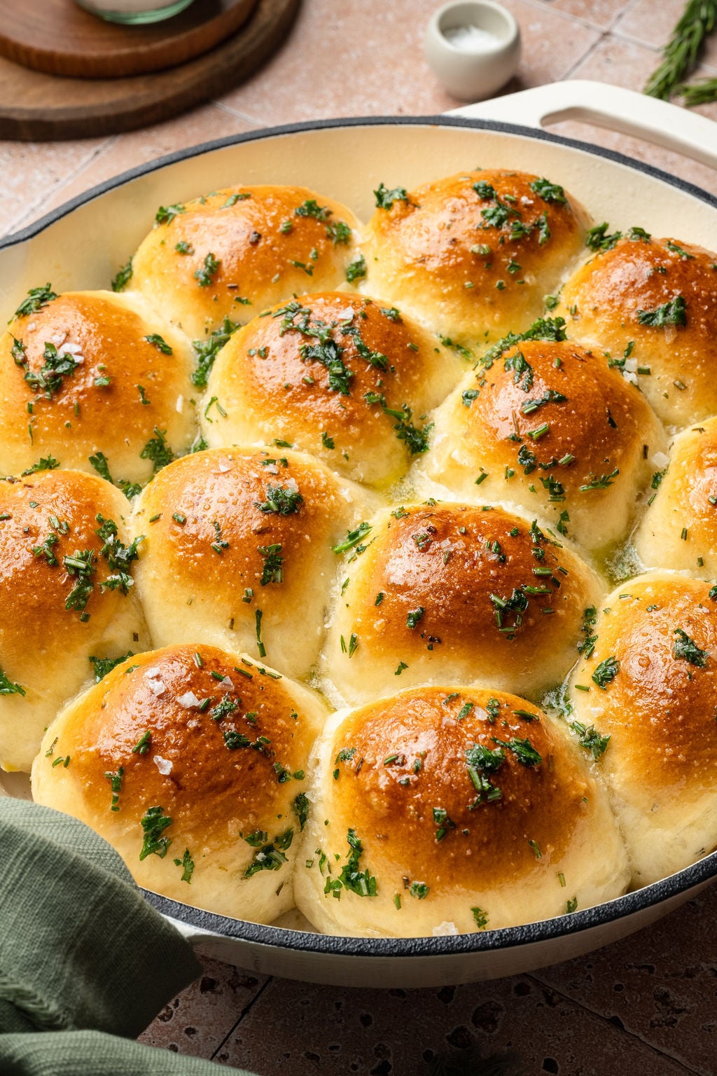 Overhead view of garlic rosemary rolls in a white skillet, baked until golden brown and finished with flaky sea salt and herbs.