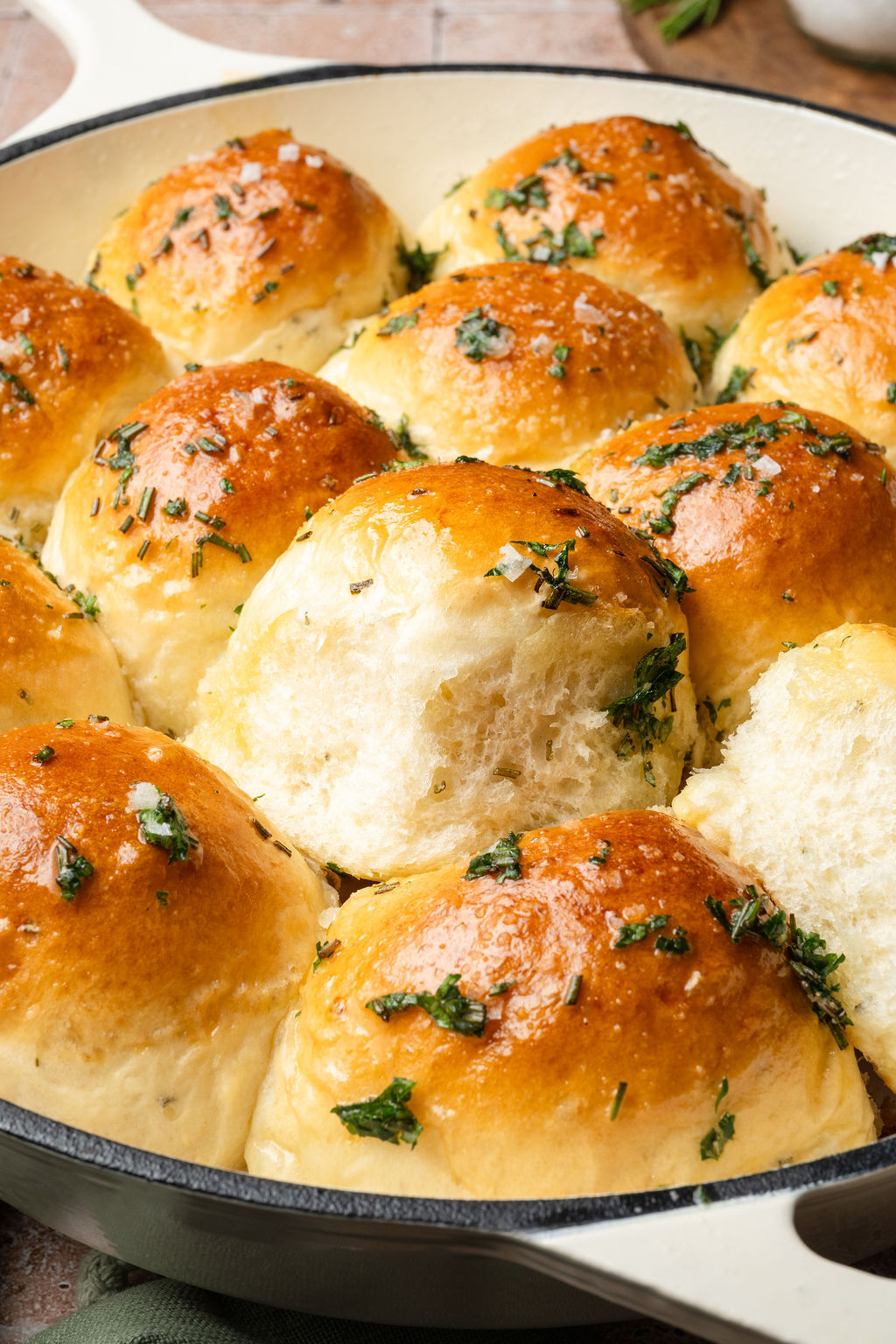 Garlic rosemary dinner rolls with one roll pulled out, showing the soft fluffy texture inside.