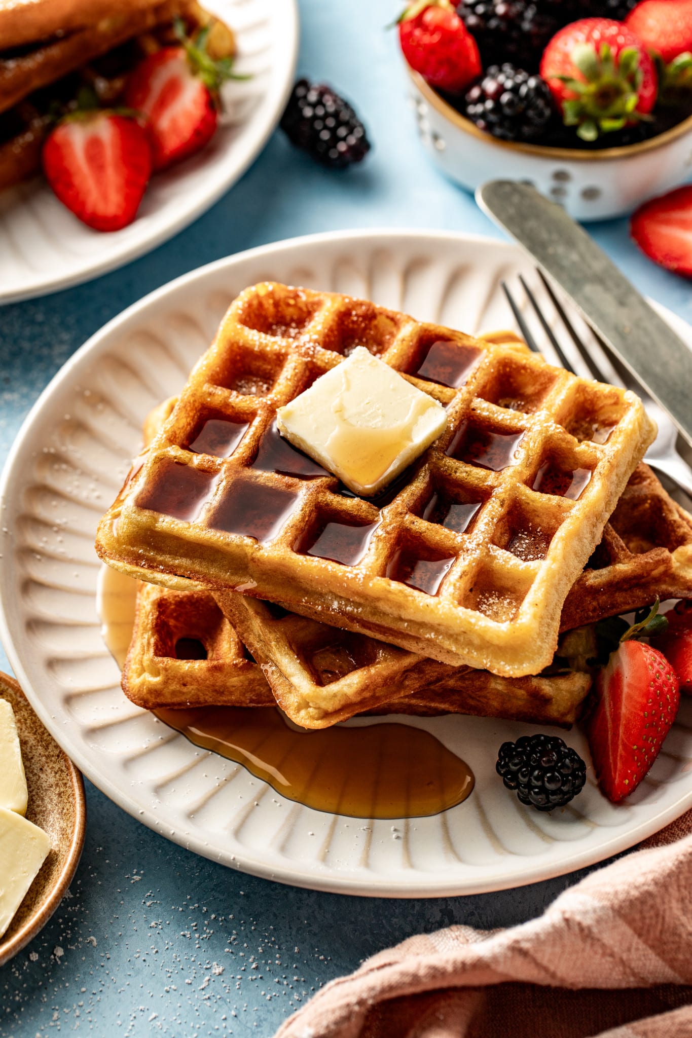 Buttermilk waffles stacked on plate topping with butter and syrup.