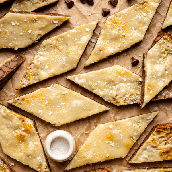 Coffee cookie bars cut into diamond-shapes on parchment paper with small bowl of flaky salt and chocolate chips.