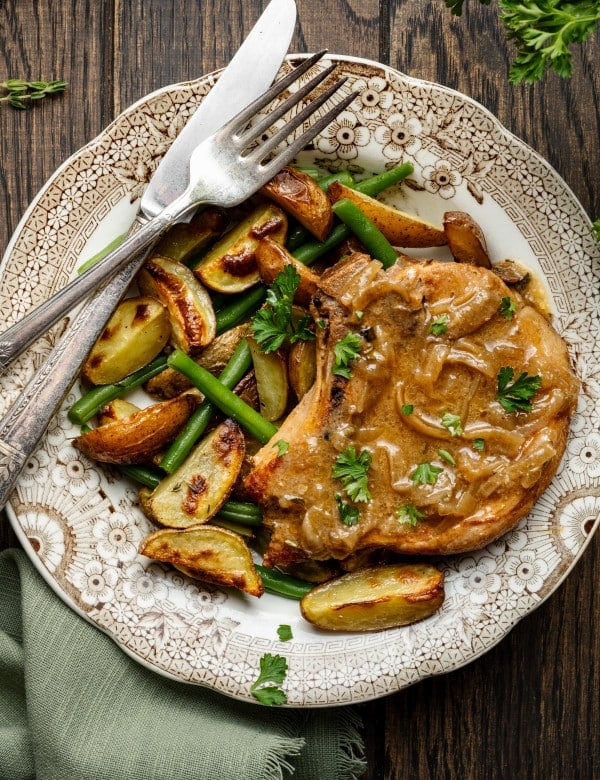 Slow cooker pork chop on plate with potatoes and green beans with knife and fork.