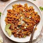 Spanish rice and chorizo on plate garnished with lime wedges and spoon on side of plate.