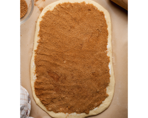 Overhead image of rolled-out cinnamon roll dough spread evenly with a thick layer of brown sugar and cinnamon filling, ready to be rolled into logs.