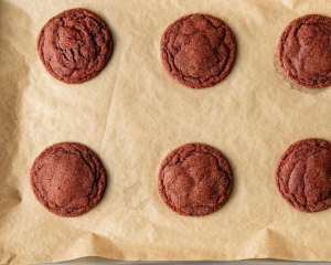 Six red velvet cookies baked on parchment-lined baking sheet.