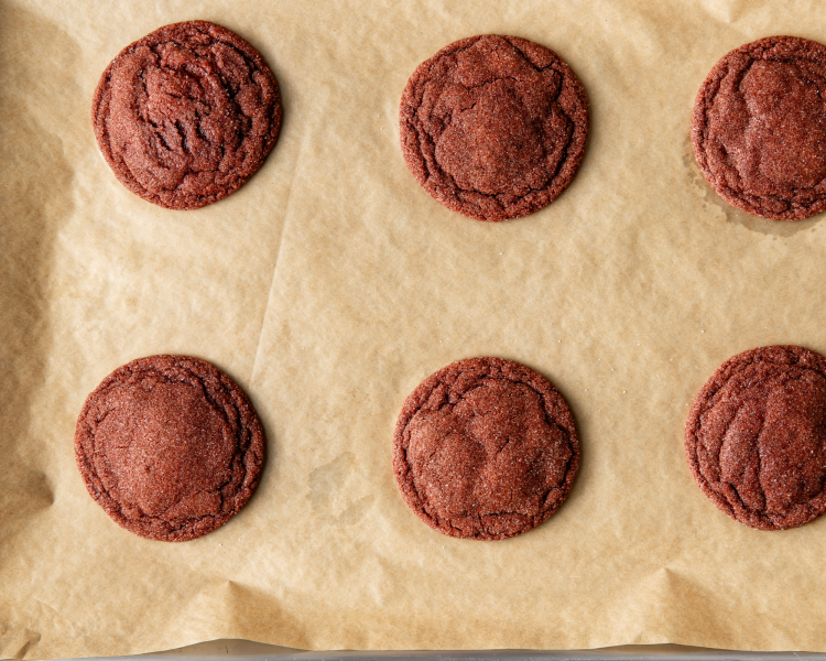 Six red velvet cookies baked on parchment-lined baking sheet.