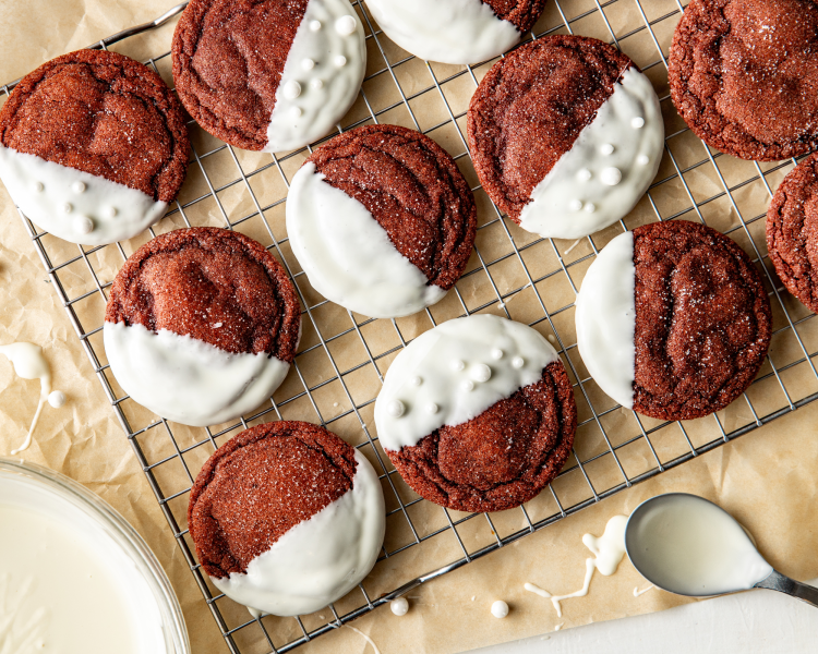 Red velvet cookies dipped in white chocolate and drying on wire rack.