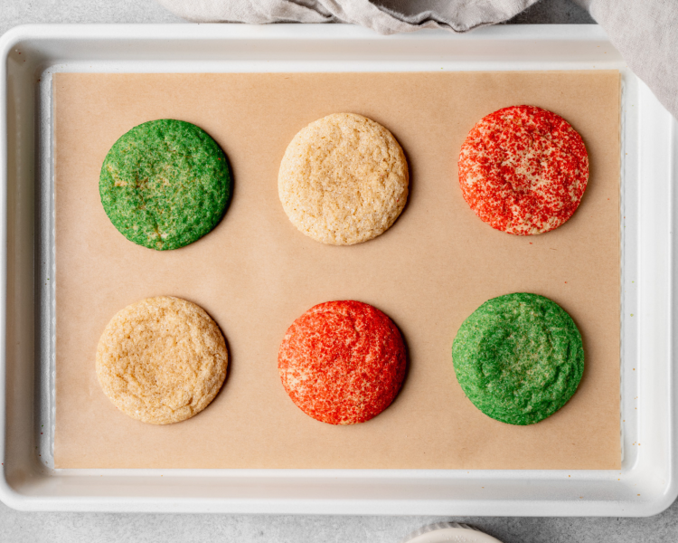 Six christmas snickerdoodles baked on parchment-lined baking tray.
