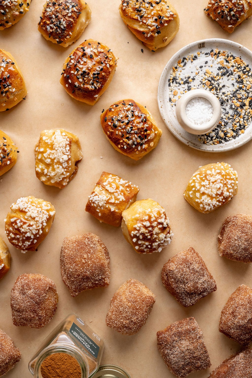 Overhead view of baked pretzel bites in three flavors—cinnamon sugar, salted, and everything bagel—spread across a parchment-lined surface.