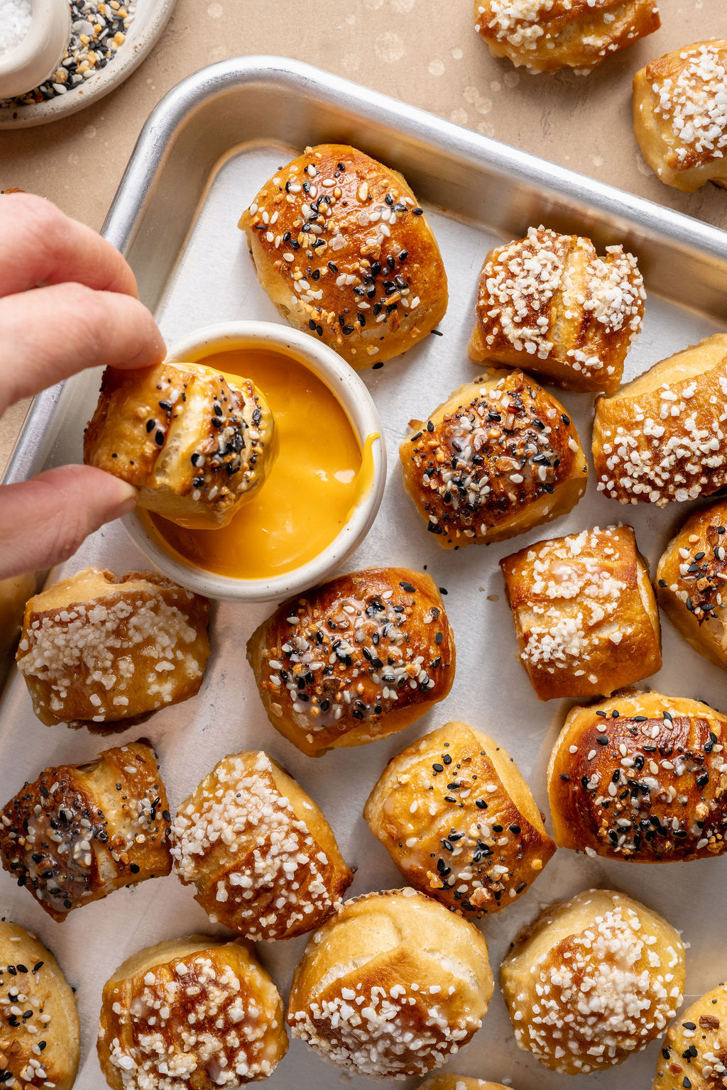 Overhead view of a hand dipping a warm pretzel bite topped with everything bagel seasoning into a bowl of cheese sauce.