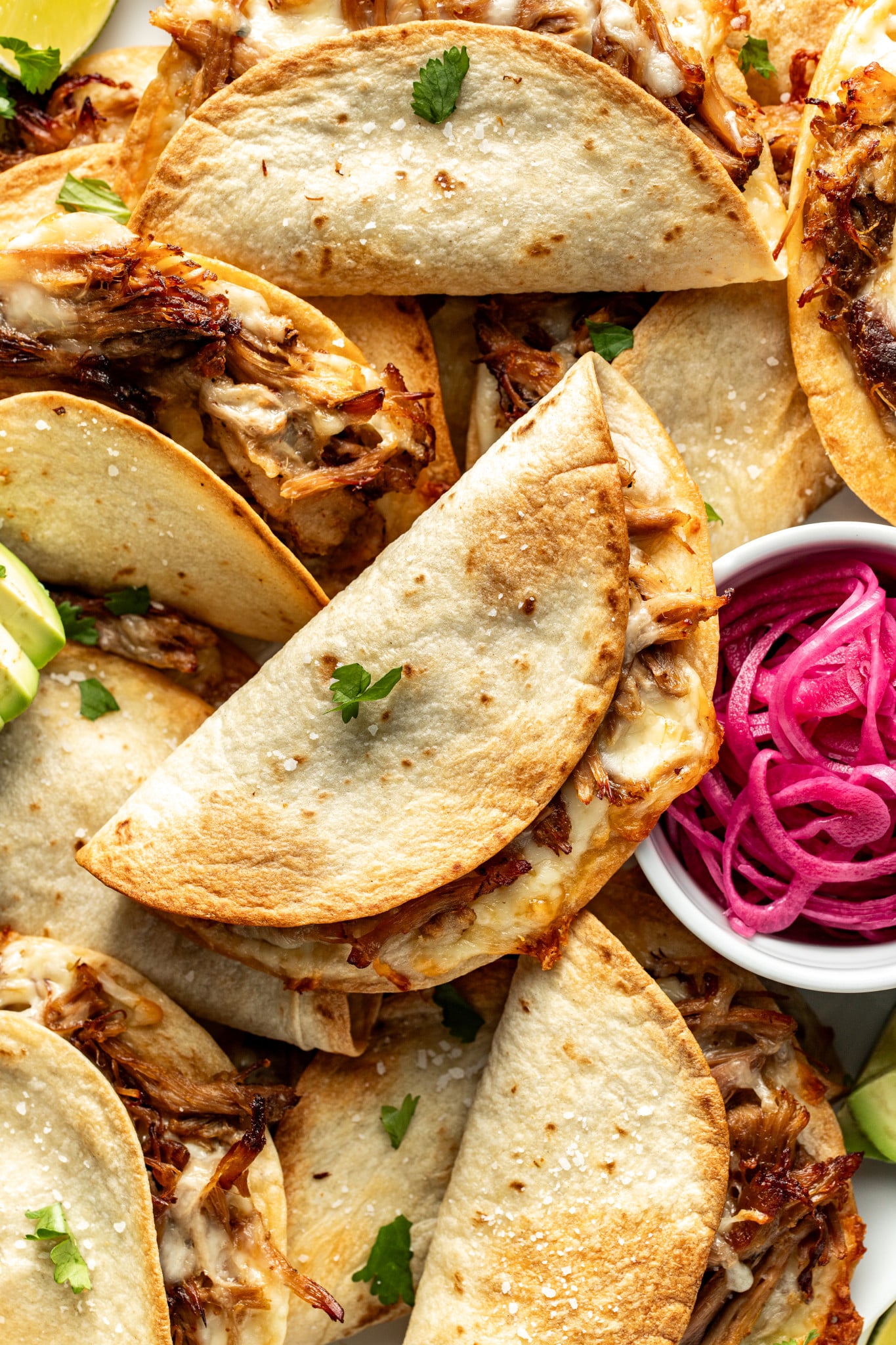 Crispy baked pork tacos piled on top of each other with small bowl of pickled red onions on the side.
