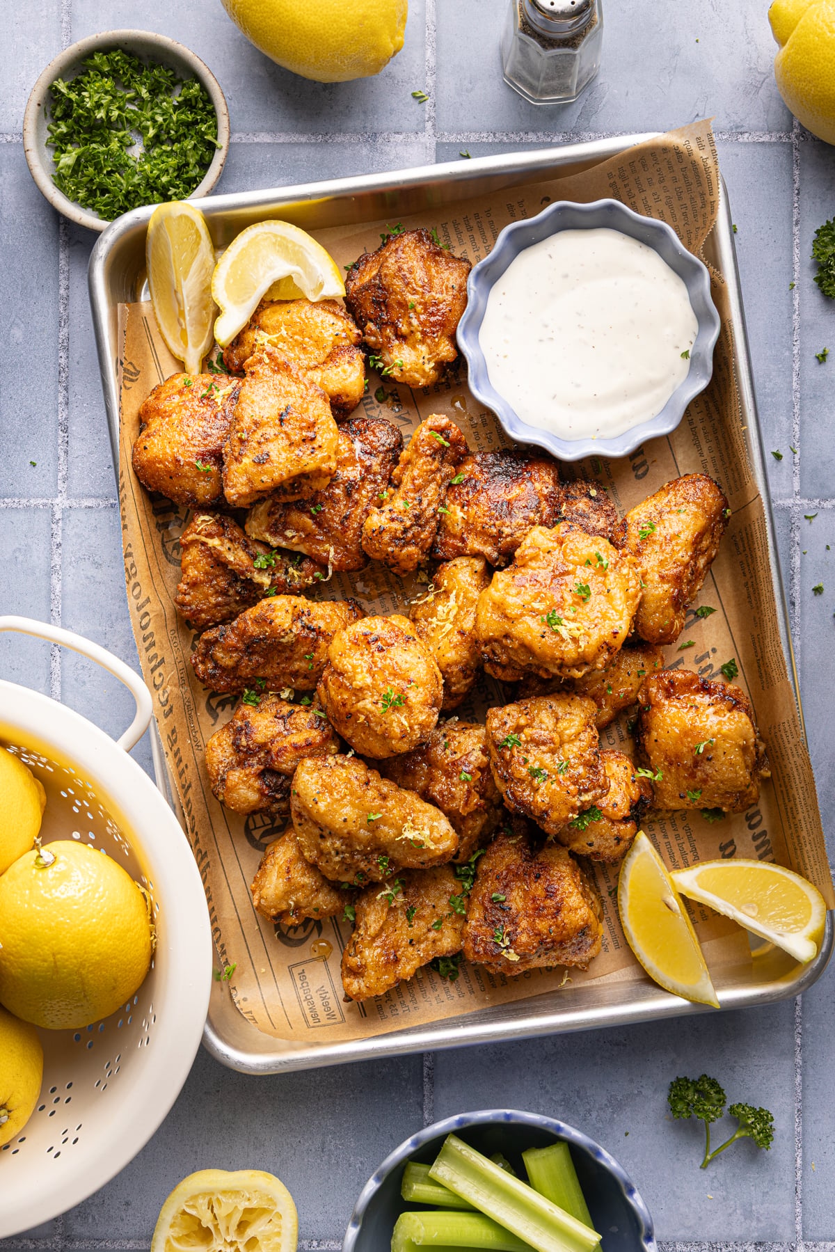 Lemon pepper boneless chicken wings cooked and placed on parchment-lined baking sheet garnished with fresh parsley and lemon wedges.