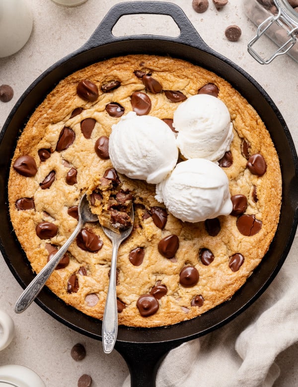 Chocolate chip cookie skillet topped with three scoops of vanilla ice cream and two spoons digging into the center.