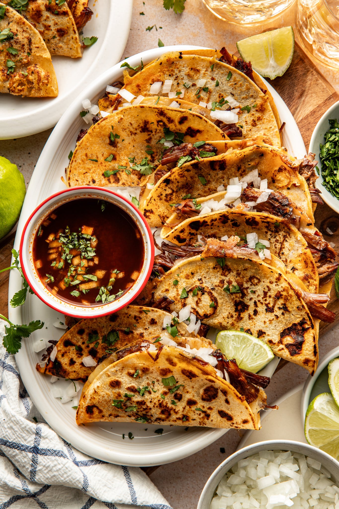 Birria tacos cooked and arranged on serving plate with bowl of consomé on side to dip.