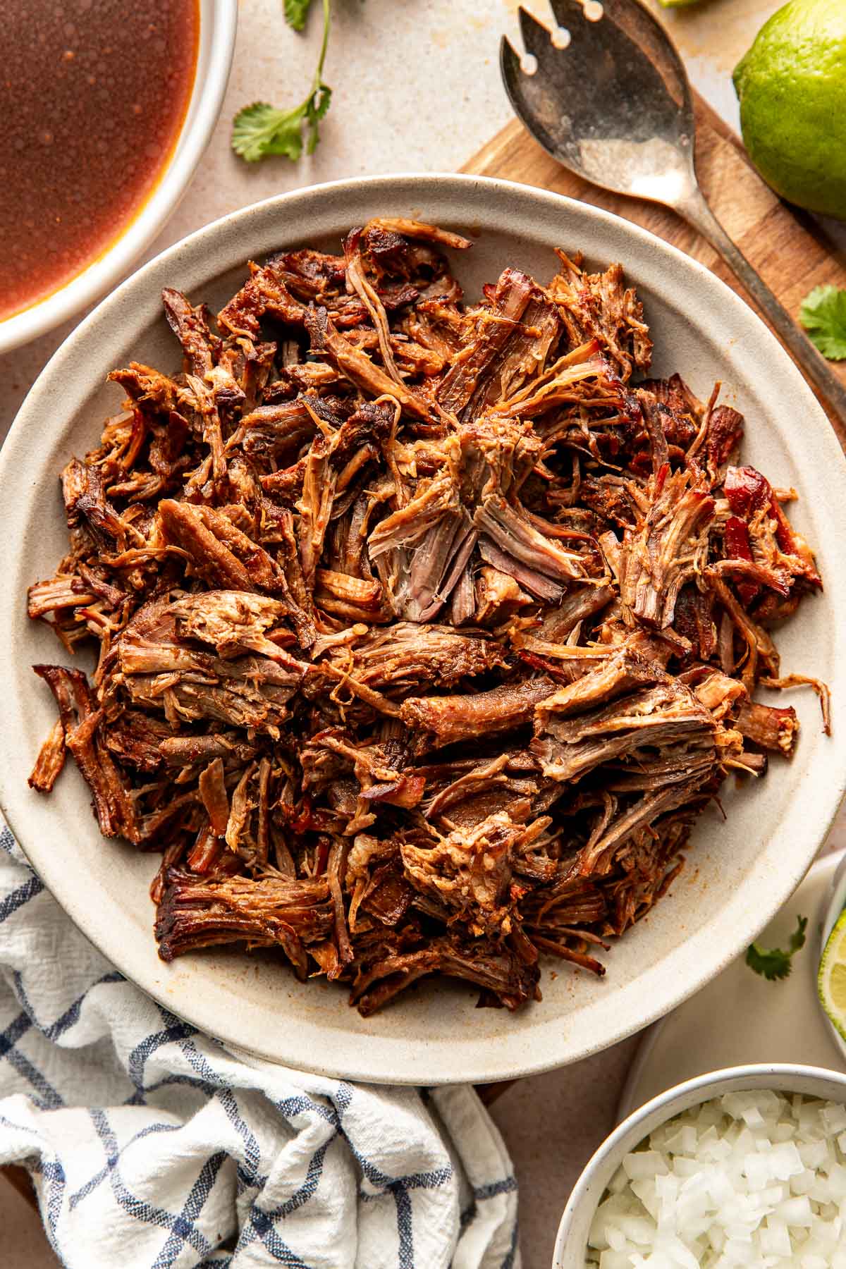 Close-up overhead shot of shredded birria beef in a serving bowl, highlighting the moist, tender texture and deep brown-red color.