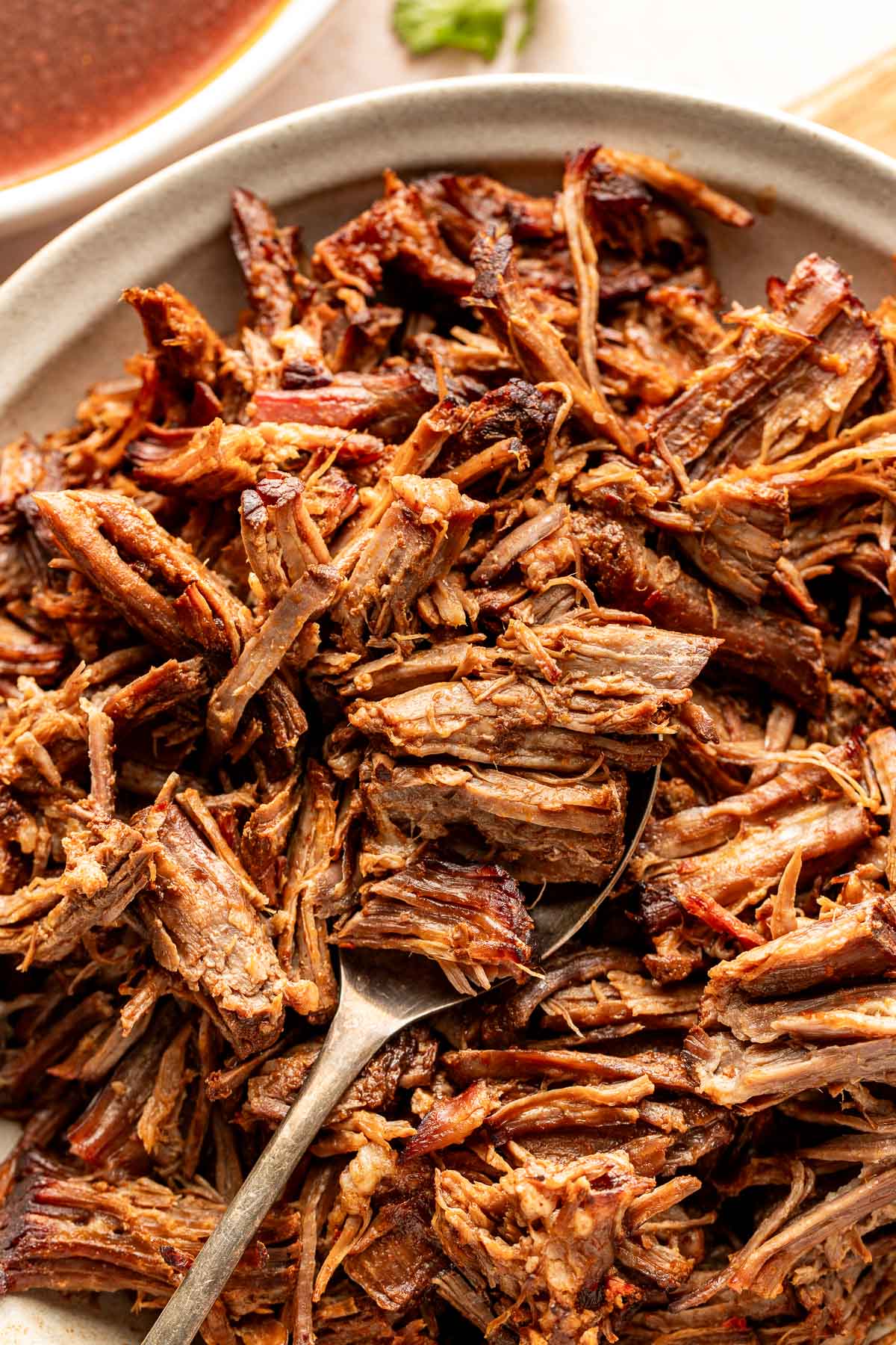 Close-up of shredded birria beef with a spoon scooping through the meat, emphasizing the juicy texture and chile-coated strands.