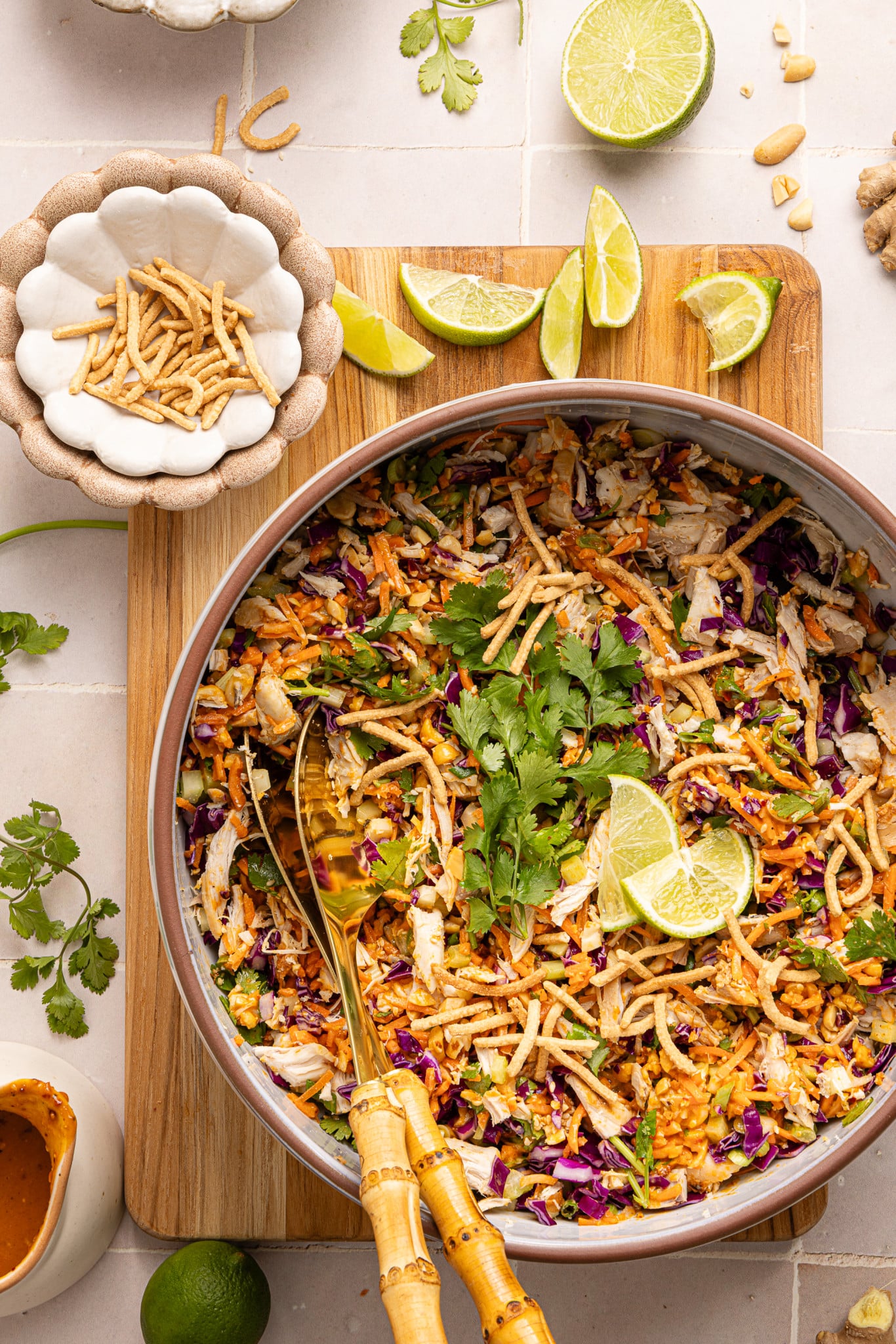 Thai chicken salad with peanut dressing in large bowl garnished with chow mein noodles and lime wedges.
