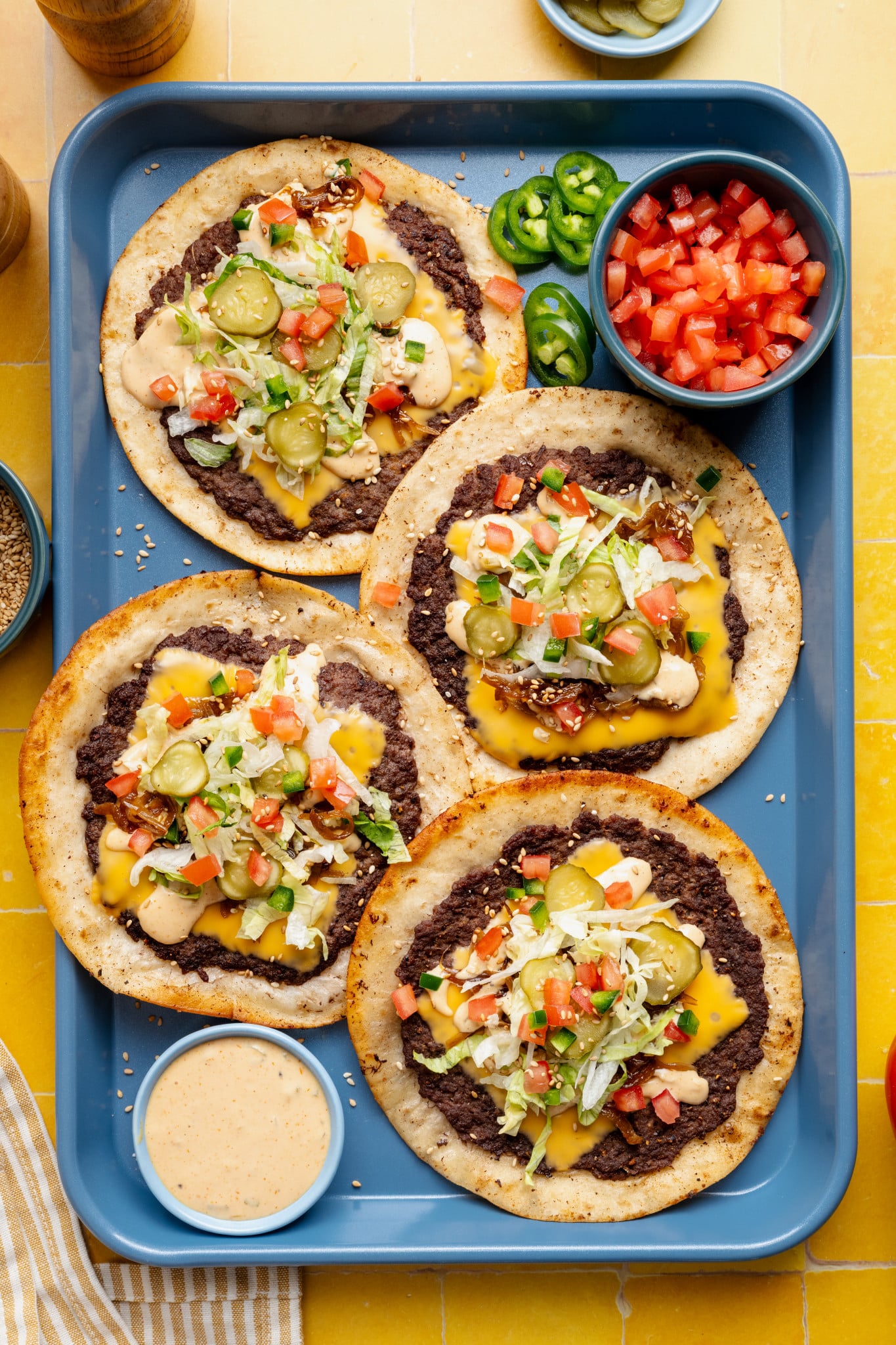 Four cheeseburger tacos with toppings added on blue food tray with burger sauce in a small bowl on the side.