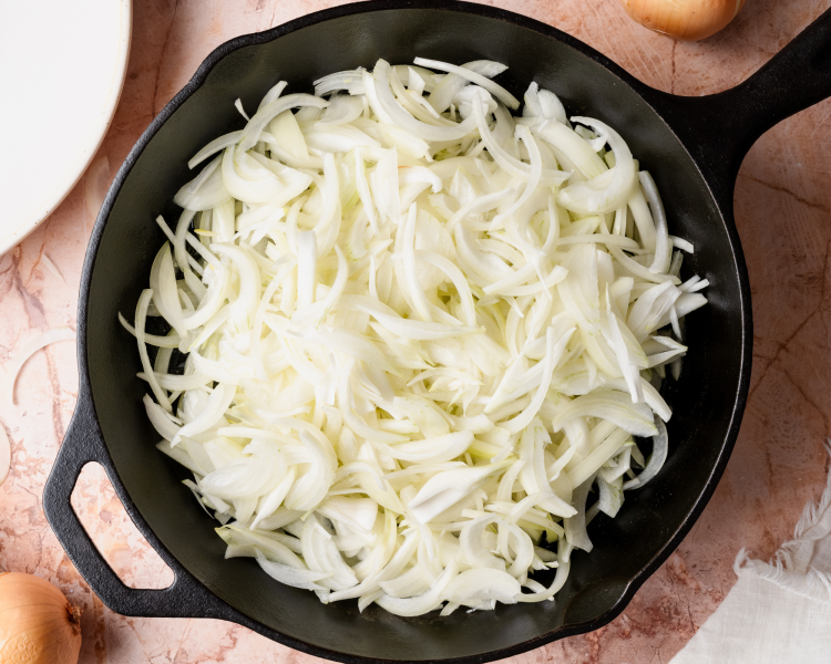 Thinly sliced onions added to cast-iron skillet.
